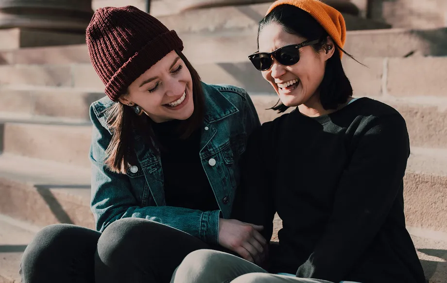 photo of two friends laughing and smiling while sitting on an outdoor staircase